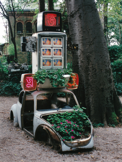 Installation view of NAM JUNE PAIK’s Marco Polo, 1993, Volkswagen car body, refrigerator, old television chassis, neon, three metal television cabinets, flowers, six Quasar televisions, laser disk player and Paik video program on laser disk, dimensions variable.